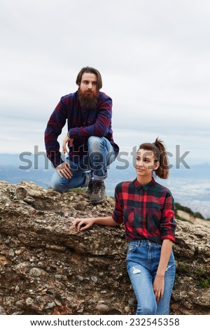 Couple of stylish hipster guys sitting on rock cliff, hiker man and woman sitting on mountain hill with beautiful horizon view on background, beautiful people at hike in nature landscape