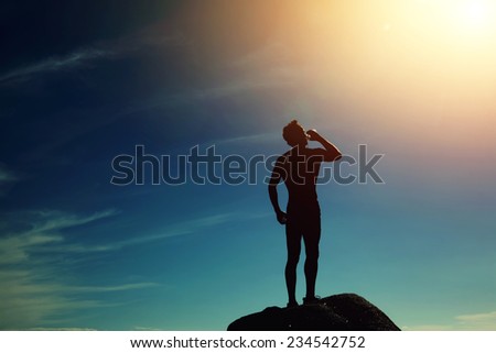 Silhouette of athlete refreshing with bottle of water after run, muscular build beautiful man drinking water after fitness outdoors,sporty fit man drinking water at sunny day standing on mountain hill