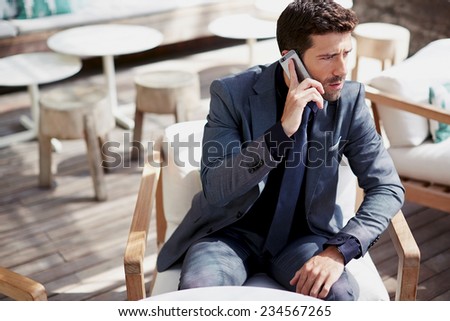 Confident businessman talking on mobile phone sitting in cafe, handsome caucasian business man in suit using mobile phone focused in the work, handsome stylish man talking on smart phone looking away