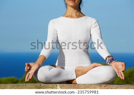 Close up woman seated in yoga pose on amazing sea background, yoga on high altitude  with sea on background, woman meditating yoga enjoying sunny evening, woman makes yoga meditation on high altitude