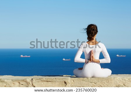 Yoga on high altitude with sea with ships on background, woman seated in yoga pose on amazing sea background, woman meditating yoga enjoying sunny evening, woman makes yoga meditation on mountain hill