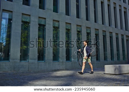 Young stylish man holding fixed gear bicycle walking in the city, handsome hipster man walking with bicycle near modern architecture building, fashion model man posing with fixed gear bicycle