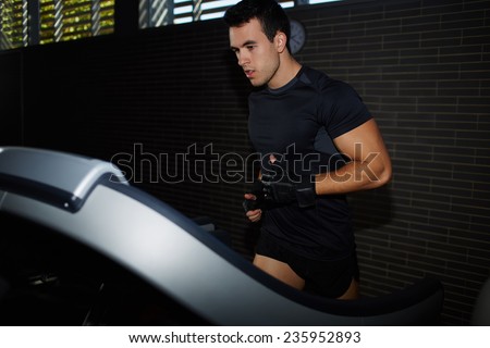 Fit man running in a gym on a treadmill looking to the screen, attractive sportsman at the gym doing exercise on the treadmill, handsome brunette man doing workout in gym running on treadmill