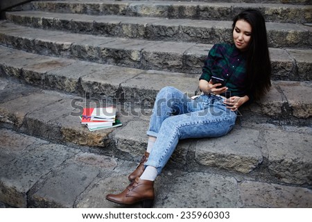 Young asian student using mobile phone during her class break at university school sitting on the steps, student girl browsing the internet with her cell phone, technology and communication concept