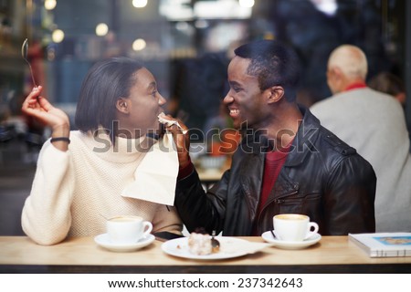 Portrait of young couple in love at a coffee shop, boyfriend wiping her mouth with a napkin at breakfast, romantic couple having fun together, two friends smiling sitting in cafe