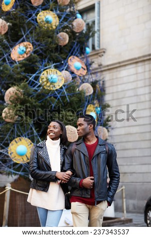 Laughing couple on christmas vacation walking in the city, beautiful young couple having fun walking on vacation holidays, romantic couple walk on christmas tree background on big square