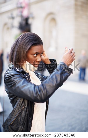 Beautiful woman making up using a smart phone as a mirror, chiming young girl looking on a mirror standing on the square