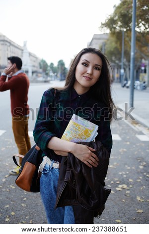 Charming asian tourist girl holding city map standing on big beautiful road, stylish hipster girl standing with city map on beautiful road covered with autumn leaves