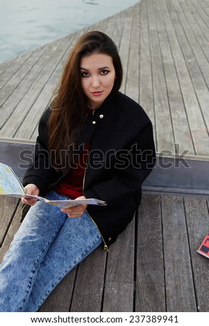 Portrait of charming asian race girl sitting with the map on wooden pier, attractive tourist girl resting after walk sitting on wooden pier in sea port,portrait of beautiful student girl with city map