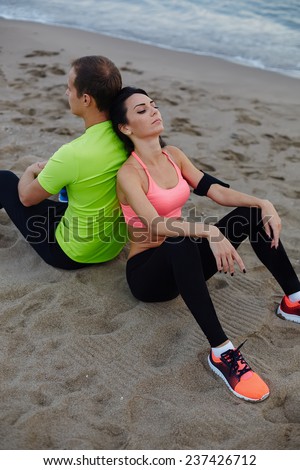 Fitness couple resting after workout sitting on the beach, exhauster after run charming woman taking break leaning on the back of boyfriend, sport couple resting after jogging outdoors sitting on sand