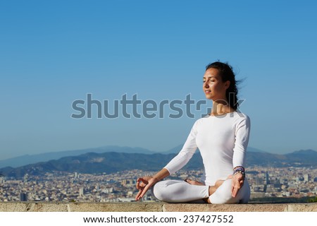 Woman meditating and exercising in yoga pose on high altitude, young woman seated in yoga pose on amazing city background , attractive girl makes yoga on mountain hill at sunset