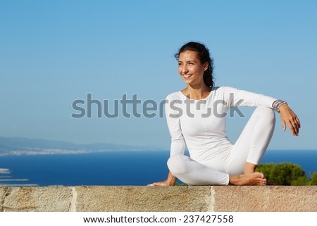 Charming young woman seated on amazing sea background resting after yoga class