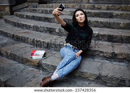 Pretty tourist girl taking a self portrait with smart phone in Barcelona, hipster girl photographing herself with phone, laughing student girl taking a self portrait with smart phone sitting on steps