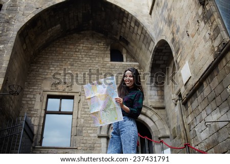 Charming tourist woman studying a map standing in gothic quarter in Barcelona, pretty young tourist girl holding city map in the hands smiling, female traveler searching right direction on city map