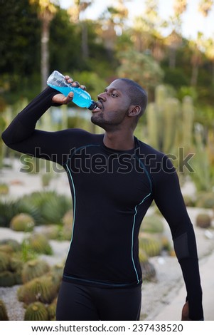 Attractive fit man in active clothes refreshing with water after run, dark-skinned healthy man with beautiful body drink water after workout outdoors, male jogger taking a break after jogging