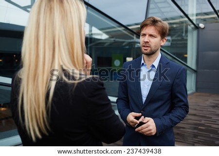 Businesswoman talking with her business partner standing near skyscraper office, confident businesspeople having serious conversation about the work, boss discussing with employee