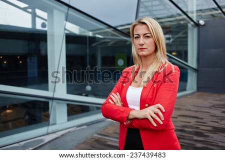 Portrait of a confident businesswoman standing against skyscraper office building, professional businesswoman with arms crossed, successful business woman looking confident