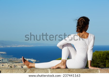 Yoga on high altitude with big city on background, young woman seated in yoga pose on amazing city background, woman meditating yoga and enjoying sunny evening, woman makes yoga on mountain hill