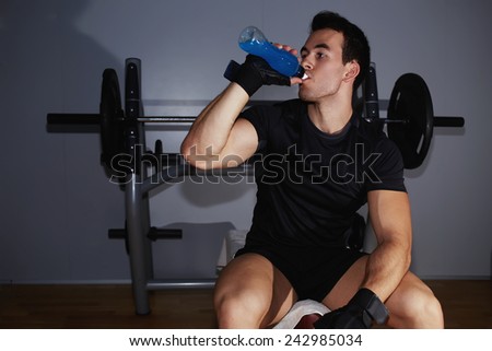 Athletic man in fitness gloves refreshing with energy drink after hard training