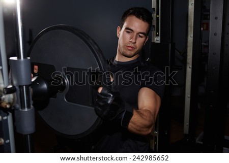 Muscular-build fit man changing weights of barbell while preparing gym equipment for began his training, athletic man preparing gym machine for workout