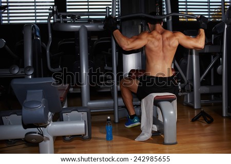 Back view of muscular build athlete exercising on pull down weight machine