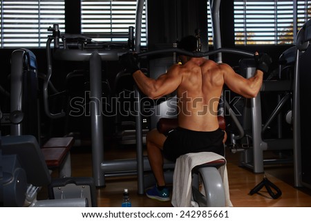 Young athlete with muscular body working out on pull down machine at gym