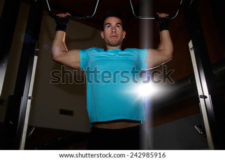 Portrait of attractive man doing exercise on pulls ups machine at gym