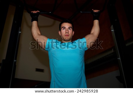 Muscular build athlete doing pull up exercise at gym, professional bodybuilder training in fitness center