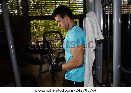 Muscular build athlete working out with lat machine dumbbells at gym