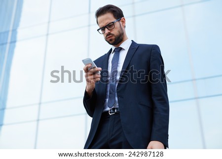 Portrait of worried young business man looking to his cell phone standing near office building