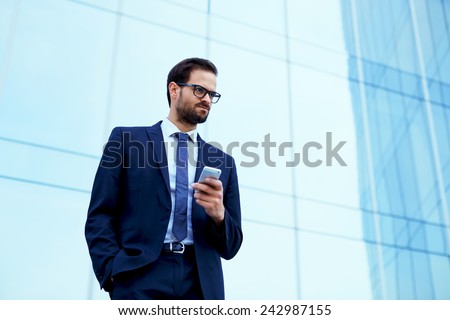 Portrait of young executive looking stressed standing near office with smart-phone in the hand