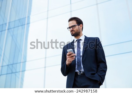 Portrait of angry business man holding his mobile phone while standing at office building