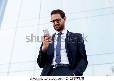 Happy businessman smiling as he reads a text message standing outside the office