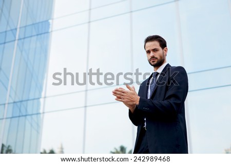 Handsome businessman in suit rubs his hands with premonition of profit, man with good feeling standing near office building