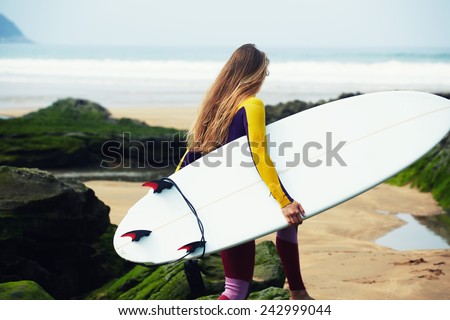 Professional female surfer walking to the ocean waves holding her surfboard, female surfer holding copy-space surfboard