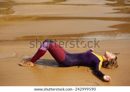Tired to surfing professional surfer girl lying on the beach feeling good and happy, female surfer in wetsuit taking a break after surfing