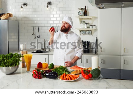 Portrait of an experienced chef holding beautiful red tomato in the hand and look to the camera