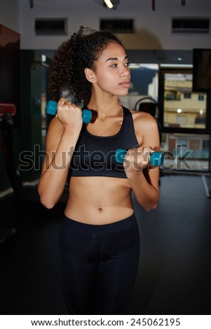 Portrait of young afro woman exercising with free weights at fitness center, attractive fitness woman doing exercise for her biceps with little dumbbells