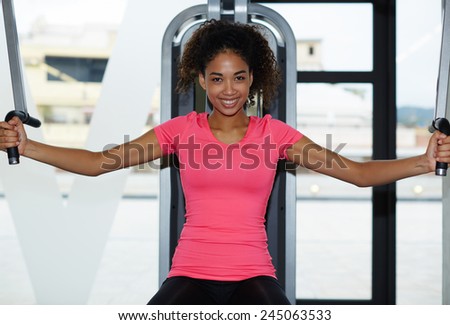 Portrait of young athletic woman exercising her chest muscles on press machine at gym, attractive fitness girl looking so happy working out