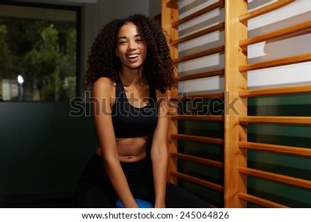 Young attractive girl with curly hair having fun at gym sitting on balance ball