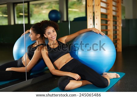 Attractive fit girl relaxing after fitness class sitting against big mirror at health center