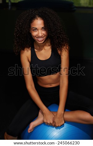 Attractive girl with curly hair sitting on balance ball smiling to the camera