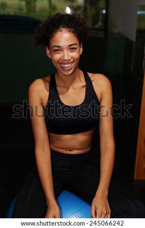 Charming afro american woman smiling brightly sitting on balance ball at gym