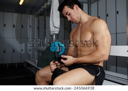 Professional athlete removing weight lifting gloves sitting in gym\'s locker room after workout