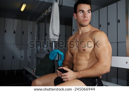 Muscular build athlete sitting in gym\'s locker room having a rest after workout