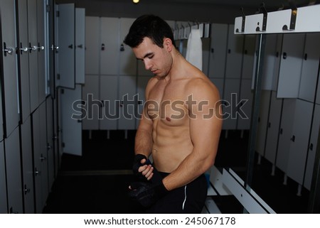 Handsome weightlifter removing lifting gloves standing in gym\'s locker room