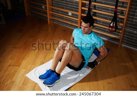 Beautiful young man in sports clothing exercising his abs and legs muscles while lying on fitness mat