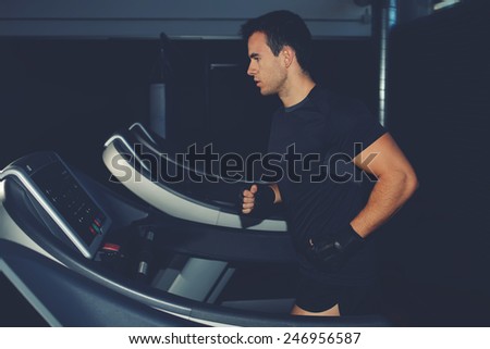 Fit man running in a gym on a treadmill looking to the screen, attractive sportsman at the gym doing exercise on the treadmill, handsome brunette man doing workout in gym running on treadmill