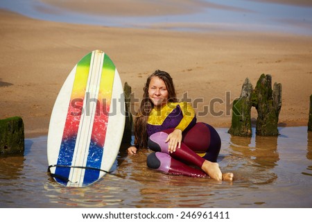 Surfer girl laughing enjoying the sun, tired to surfing female surfer lying on the wet sand looking to the camera