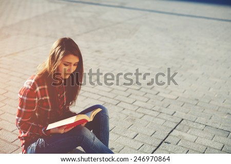 Side view portrait of attractive young girl enjoying a good book sitting at sunny evening outdoors